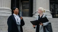 Smart young multiracial female lawyers talking about case standing near aged court building with columns before trial