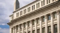 US Department of Agriculture building with Washington Monument behind, blue sky with clouds.