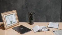 A lawyer's desk featuring a justice statue, diploma, laptop, magnifying glass, and documents.