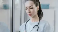Portrait of a female doctor in a disposable gown using a smartphone in a hospital environment.