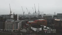 Foggy day in London featuring construction cranes over the cityscape in a moody atmosphere.