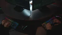 Two people typing on RGB keyboards with code on screens, indicating a cybersecurity environment.