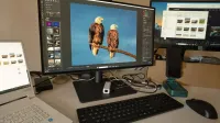 A desk setup showing photo editing software on multiple monitors, a keyboard, and peripherals.