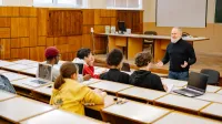Students engaging with a professor in a university lecture hall, utilizing technology.
