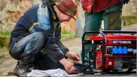 Two technicians working on a red HÜTTENBERG power generator outdoors.