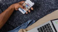 Mano que sostiene el smartphone con la computadora portátil abierta, que muestra el estilo de vida digital moderno.
