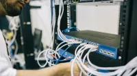 Un profesional de TI configurando cables de red en un rack de servidores, centrándose en las conexiones Ethernet.