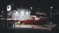 Illuminated Canadian icebreaker ship docked in a harbor at night with city lights in the background.