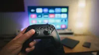 Close-up of a person holding a gaming controller in a cozy living room setup with TV.