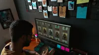 A young man edits photographs on a computer in a cozy home office setup.