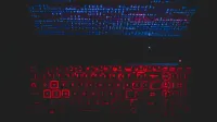Dark-themed laptop setup with a red glowing keyboard and code on screen, ideal for tech enthusiasts.