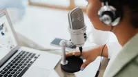 Professional woman recording a podcast or broadcast using a microphone and laptop at a desk.