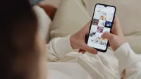 Persona que usa smartphone para navegar por Instagram en interiores, mostrando el compromiso de las redes sociales.
