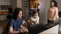 Students using laptops in a classroom setting with a teacher supervising, promoting digital education.