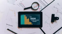 Flat lay of tablet showing 2020 stock market crash with charts and papers.
