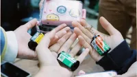 A close-up of hands holding various film roll keychains with a playful camera case.