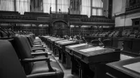 Foto en blanco y negro de una cámara de asamblea legislativa tradicional, con asientos y escritorios vacíos.