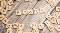 Alphabet tiles arranged to spell 'fraud' on a wooden surface, symbolizing deception.