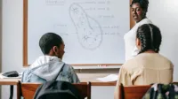 Back view of diverse children at desk listening to black female teacher at whiteboard during biology lesson