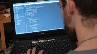 Man working on code on a laptop in an office, showcasing modern remote work setup.