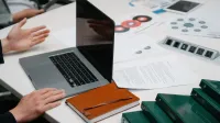 Primer plano de una mesa de reuniones de negocios con una computadora portátil, documentos y discusión en curso.