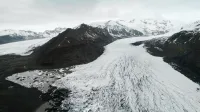 Stunning aerial view of a vast glacier surrounded by snow-capped mountains and icy terrain.