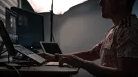 Un hombre editando fotos en múltiples pantallas en un escritorio con poca iluminación.