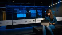 Woman using a laptop in a server room, showcasing modern technology and work environment.