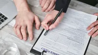 Imagen de cerca de dos personas firmando un documento de póliza de seguro en un escritorio de madera.