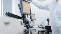 Researcher in PPE reviews data on a digital screen in a modern laboratory setting.