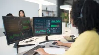 Woman analyzing financial data on dual screens at an office desk.