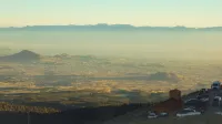 Aerial view of a city in a valley, with smog and distant mountains creating a serene landscape.