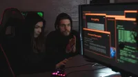 Cybersecurity experts in hoodies analyzing encrypted data on computer screens in an indoor setting.