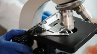 Imagen de primer plano de la mano enguantada de un científico ajustando un microscopio en un laboratorio de investigación.