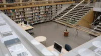 Amplio interior de la biblioteca universitaria con estanterías, escritorios y una escalera para estudio e investigación.
