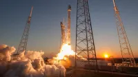 Low angle of modern rocket taking off into cloudless sky during beautiful sunset over space factory