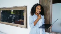 A woman enjoying remote work outdoors, wearing headphones and holding a laptop.
