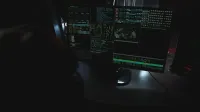 Dark room setup with code displayed on PC monitors highlighting cybersecurity themes.