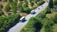 Aerial shot of a highway with trucks and cars surrounded by lush greenery.