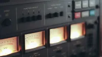 Primer plano de una grabadora de cinta vintage con medidores VU iluminados y controles de función.