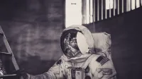 Astronaut in spacesuit climbing ladder inside a dark setting.