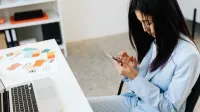 Mujer asiática en un traje azul con smartphone en el escritorio de oficina con muestras de ordenador portátil y de color.