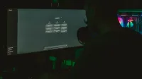A man using a computer with a large screen in a dark room, focused on technology.