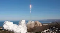 Un cohete se lanza sobre el océano, dejando atrás rastros de humo y fuego. Telón de fondo escénico con cielos despejados.