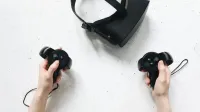 Two hands hold virtual reality controllers above a VR headset, showcasing modern technology.