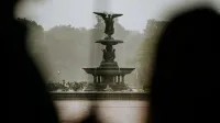 A beautiful angel statue fountain in a lush park during rainfall, creating a serene ambiance.