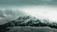 Stunning view of snow-covered mountain peaks engulfed by swirling clouds under a dramatic sky.