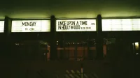 Outdoor view of an illuminated theater marquee displaying movie titles at night.