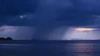 A breathtaking view of rain clouds looming above the calm ocean during twilight, creating a serene seascape.