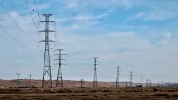 Transmission towers in a desert landscape with blue skies, showcasing energy infrastructure.